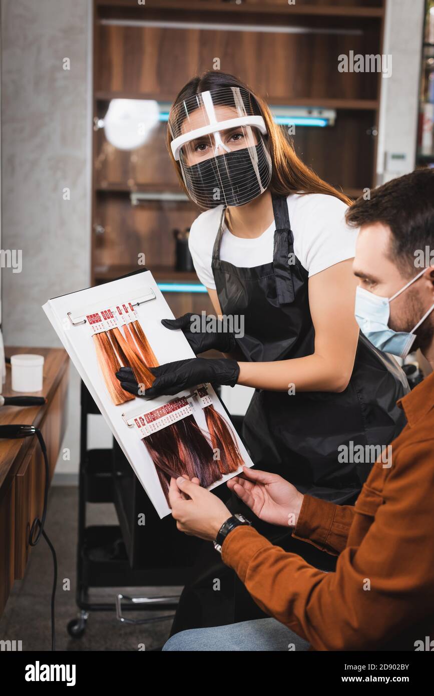 Friseur in Gesichtsschutz Blick auf Kamera, während Haare zeigen Farbpalette an Client Stockfoto