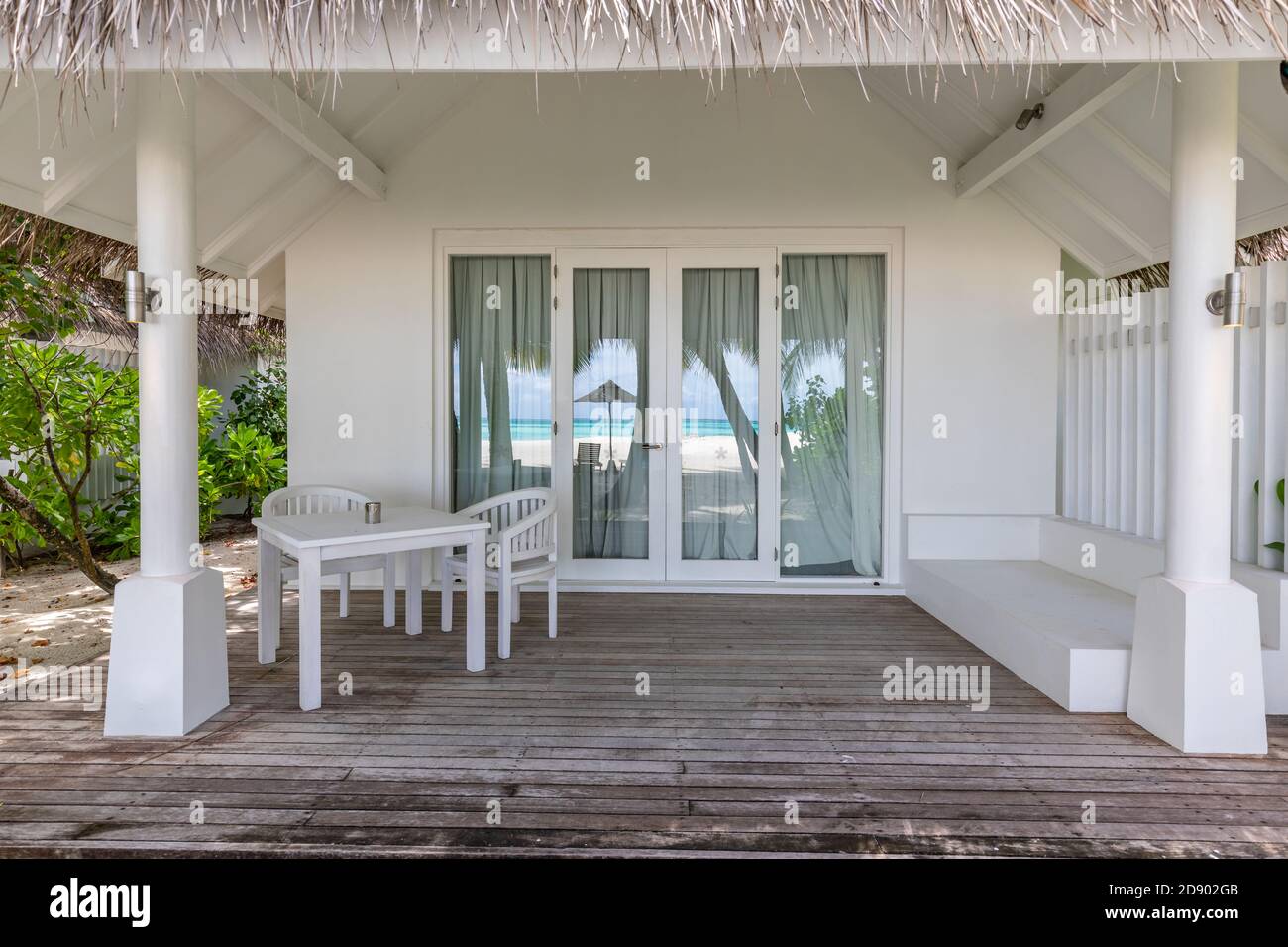 Luxusvillen am Strand. Moderne Holzterrasse, weiße Stühle und Tisch, tropischer Blick auf den Bungalow Stockfoto