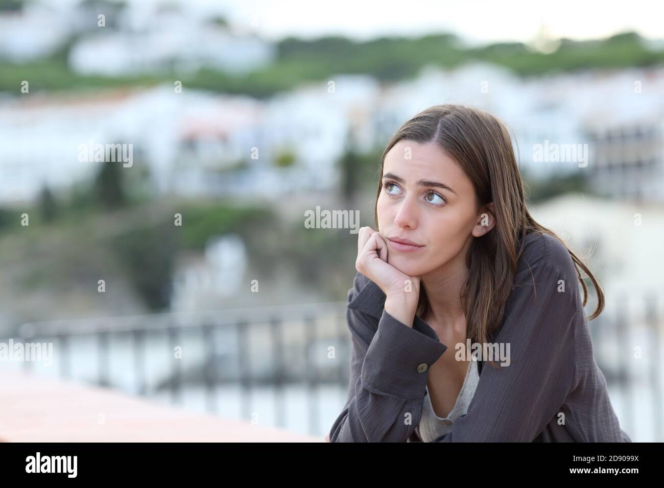 Besorgte Frau, die dachte, von einem Balkon aus auf die Seite zu schauen Eine Strandstadt im Urlaub Stockfoto