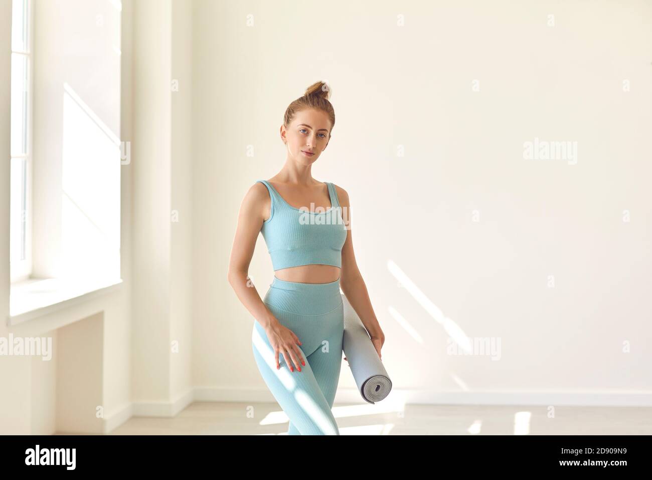Junge Frau in eng anliegender Sportbekleidung, die im Fitnessstudio Yoga hält Matte in der Hand Stockfoto