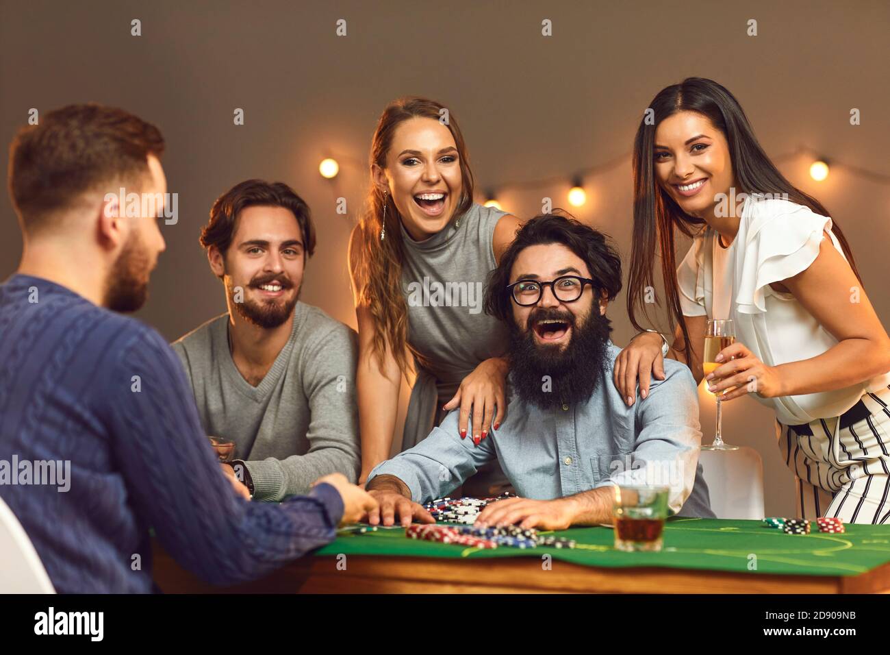 Aufgeregt Gewinner sitzt am Pokertisch von glücklichen Freunden umgeben Trinken und den Sieg feiern Stockfoto