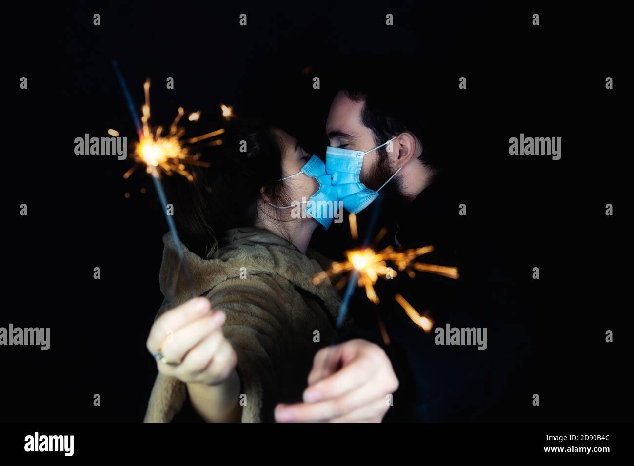 Junges Paar mit schützenden Gesichtsmasken für Coronavirus und mit Wunderkerzen für Silvester, 2021 und Covid-19 Konzept Stockfoto