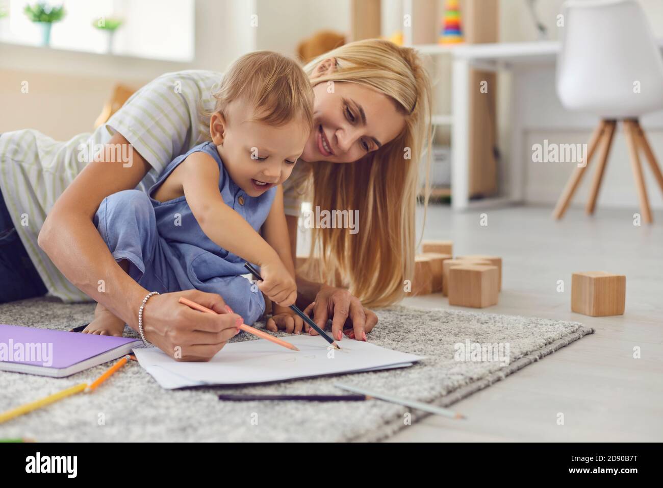 Glücklich lächelnde Frau Mutter und Baby Kind auf dem Boden sitzen Teppich und Zeichnung auf Papier zusammen Stockfoto