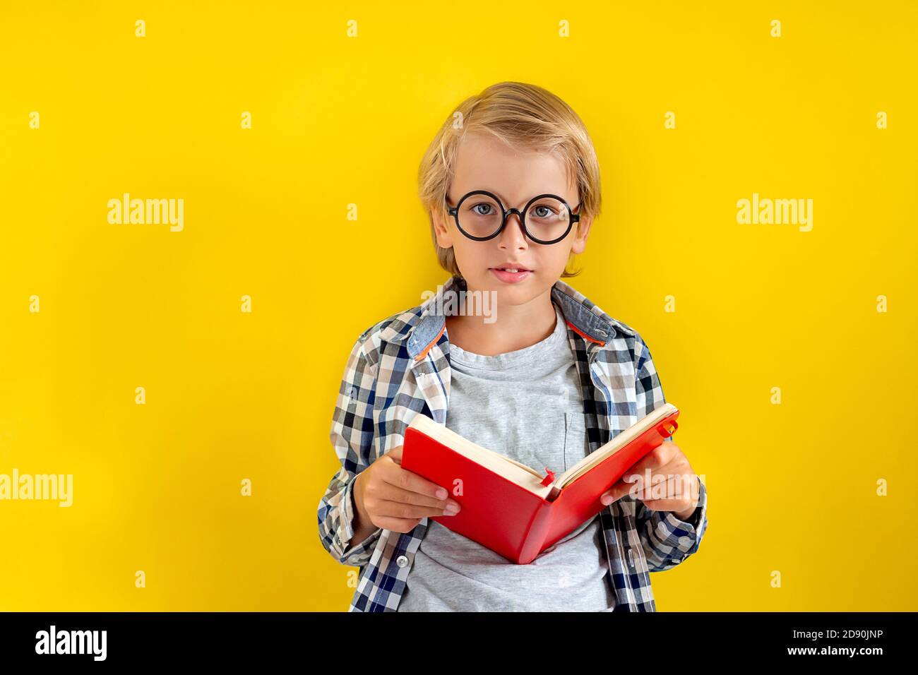 Portrait von niedlichen und cleveren blonden kaukasischen Jungen in einem karierten Hemd auf gelbem Hintergrund. September Tag. Bildung und zurück zur Schule Konzept. Kind Stockfoto