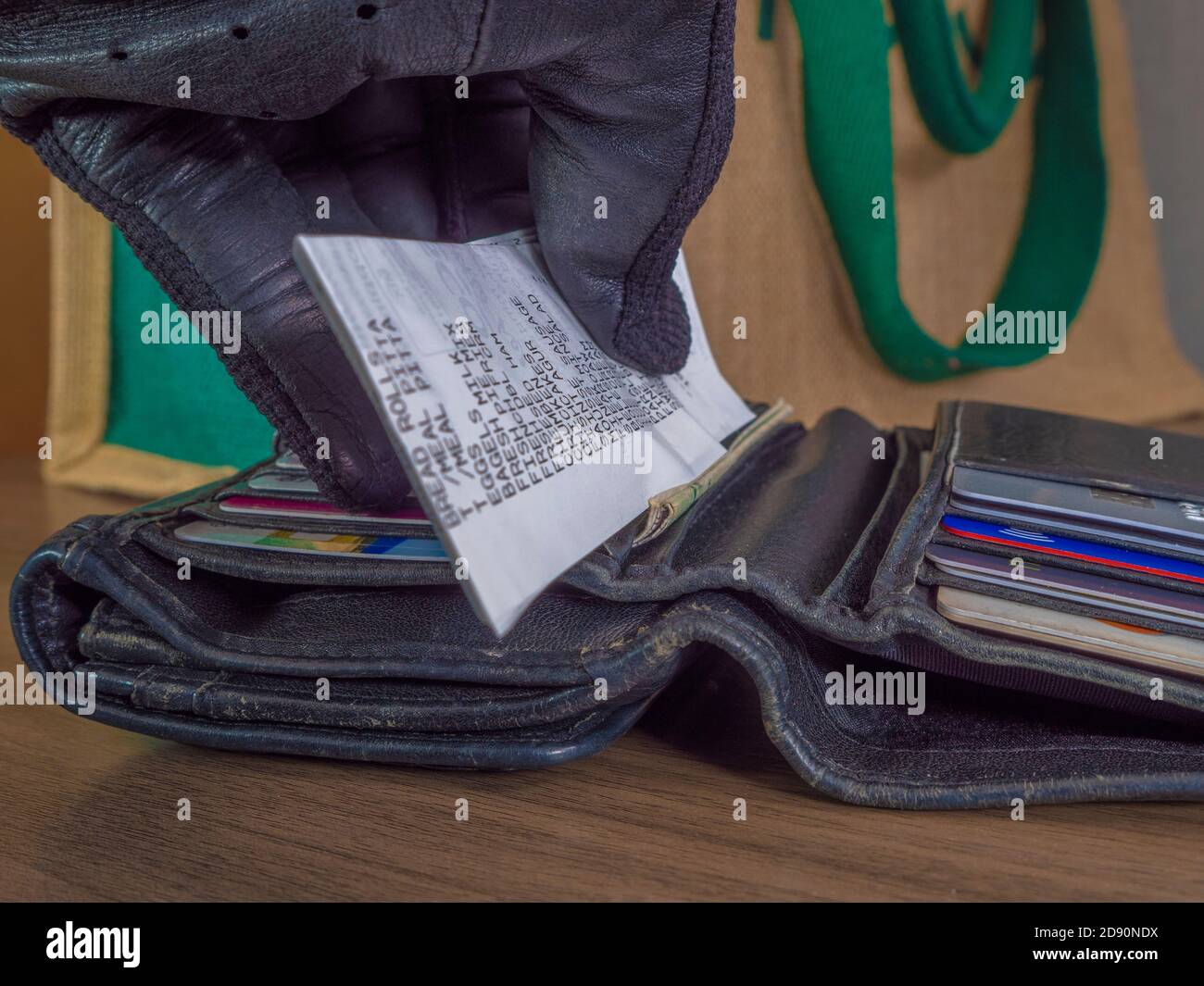 Nahaufnahme POV-Aufnahme der Hand eines Kunden, die einen Einkaufsbeleg in eine offene Ledertasche vor einer Leinentasche legt. Stockfoto