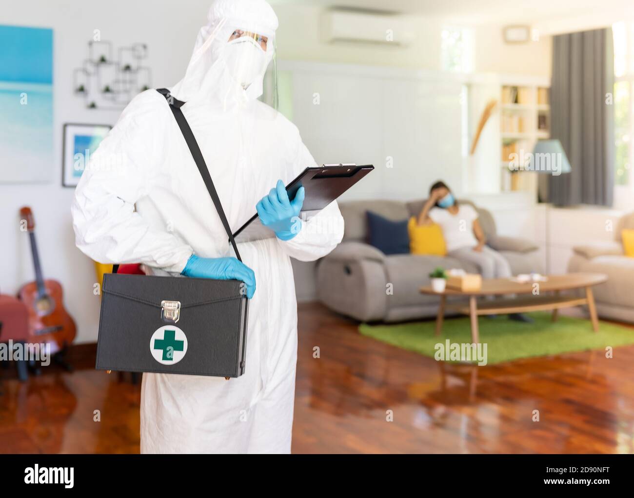 Porträt des medizinischen Personals in PSA-Anzug mit Hintergrund asiatische Frau mit Gesichtsmaske wartet im Wohnzimmer von Lieferung coronavirus covid-19 Stockfoto