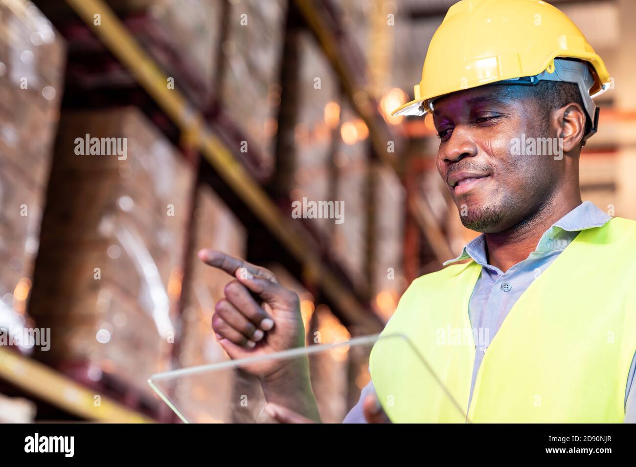 Portrait des afrikanischen schwarzen Lagerarbeiters Halten Sie Tablet und berühren Sie auf dem virtuellen Bildschirm vor ihm in großen Lagerverteilungs-Umgebung. Verwenden Stockfoto