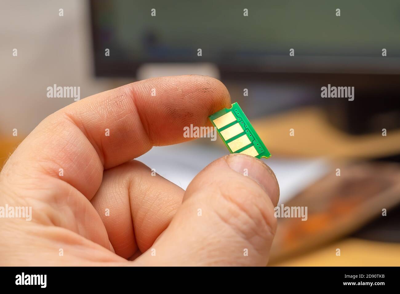 Nahaufnahme, Mikrochip mit Kupferkontakten in der Hand einer Person auf dem Hintergrund eines Monitors, Computer Stockfoto
