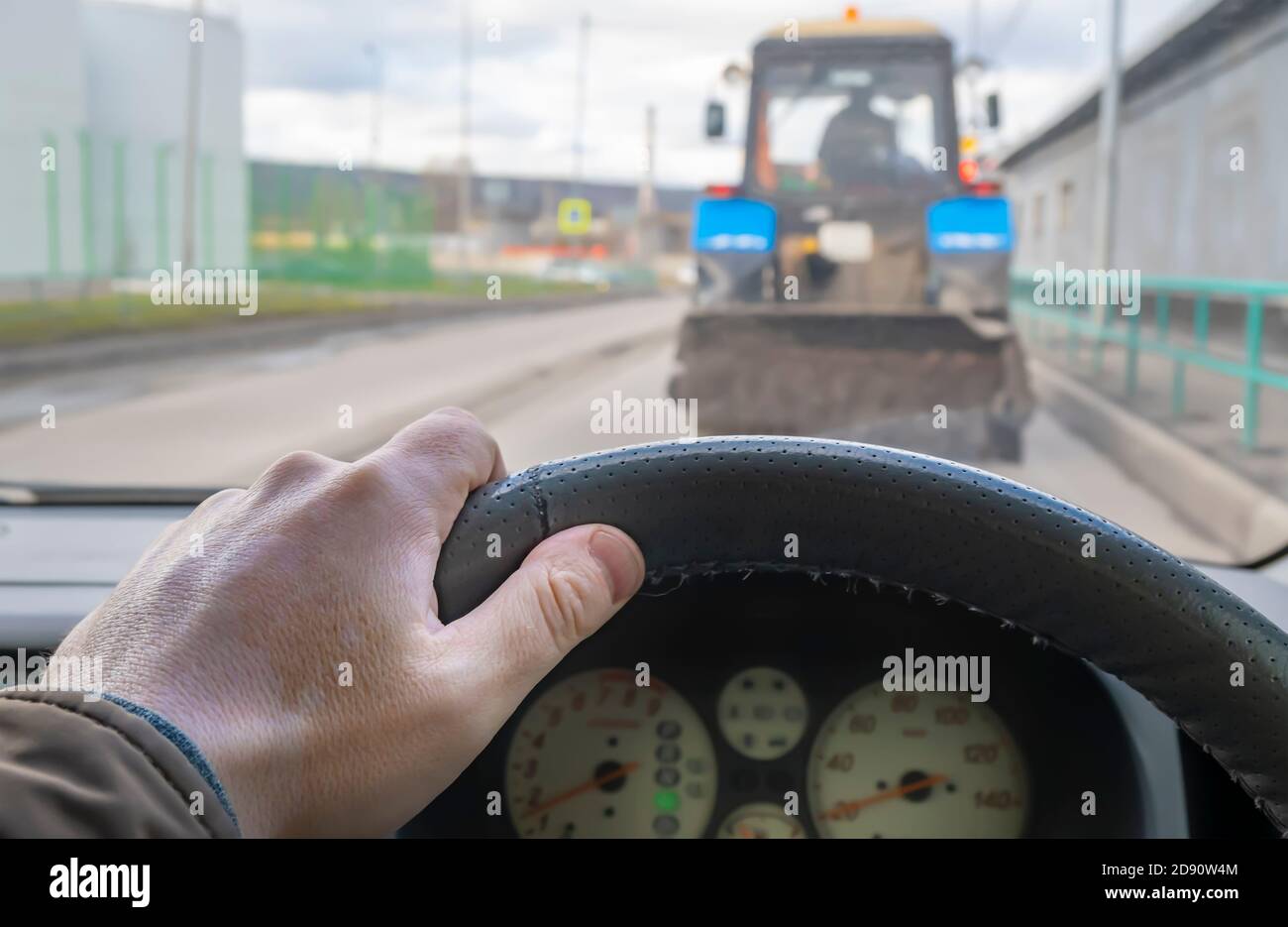 Die Hand des Fahrers am Lenkrad eines Autos, das in einem Stau auf der Straße unterwegs ist, macht ein Manöver, um den Traktor zu überholen Stockfoto