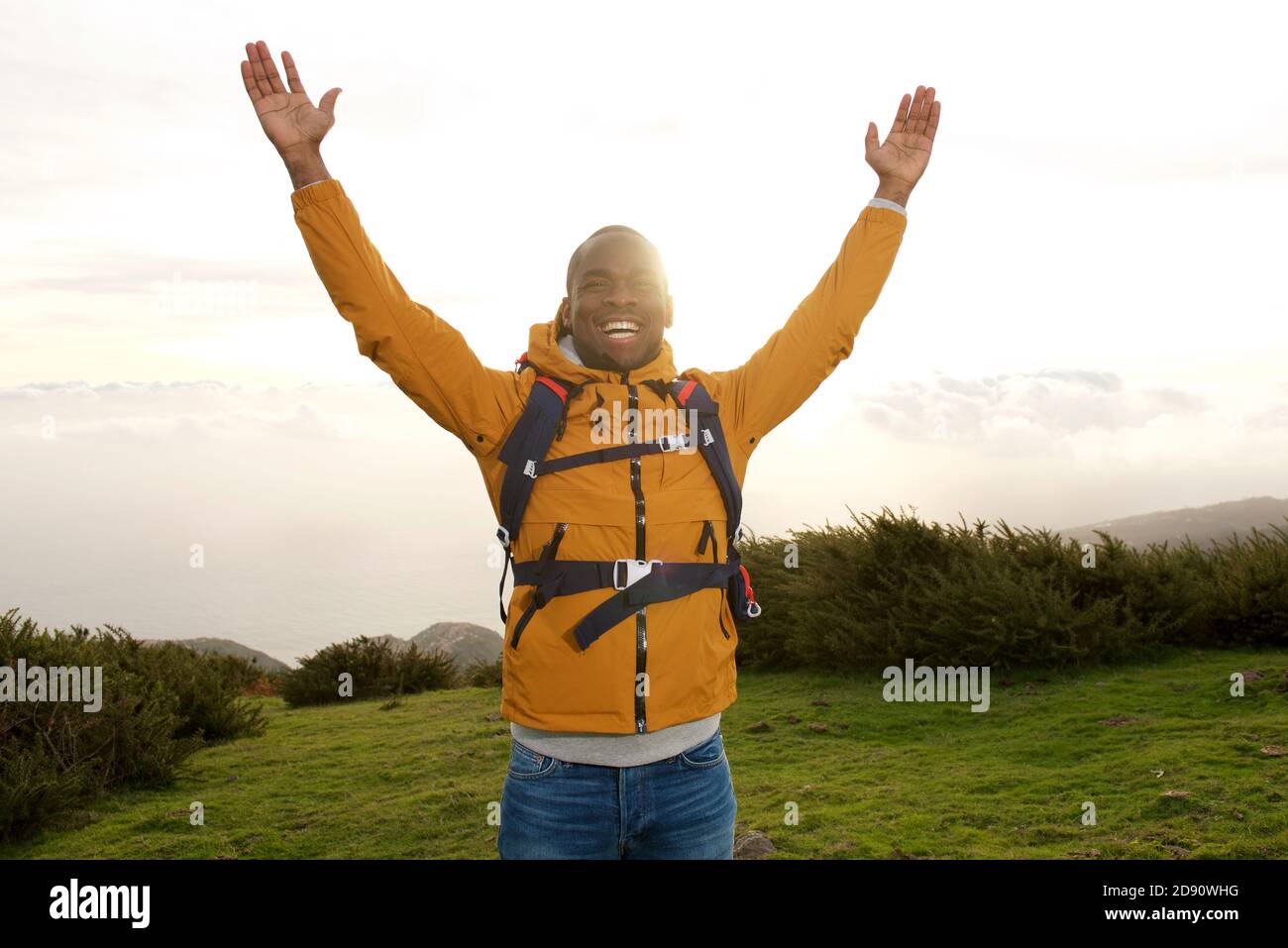 Porträt eines glücklichen afroamerikanischen Rucksacktouristen, der mit Händen im Freien steht Erhöht Stockfoto