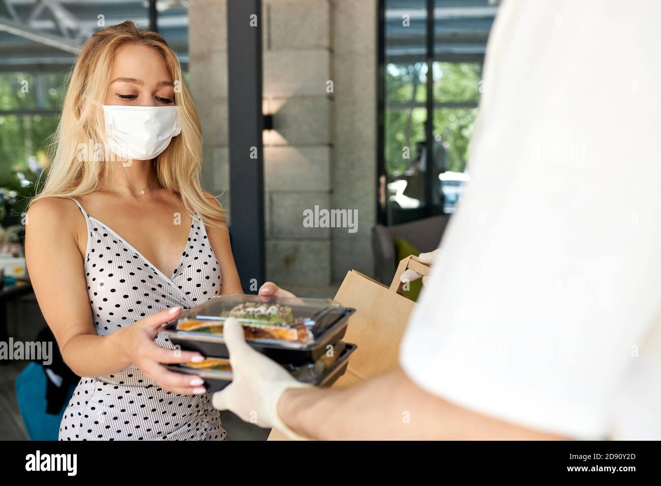 Liebenswert Frau Kunde nehmen ihre Bestellung im Restaurant während Coronavirus, Kellner des Cafés geben Essen in Behälter tragen Schutzhandschuhe, Frau ist in medizinischen Maske Stockfoto