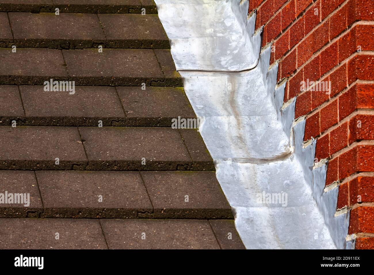 Stufenleiter blinkende Dachrinnen schaffen eine wasserdichte Abdichtung Zwischen Dachziegel und Ziegelwand auf einem Haus Stockfoto