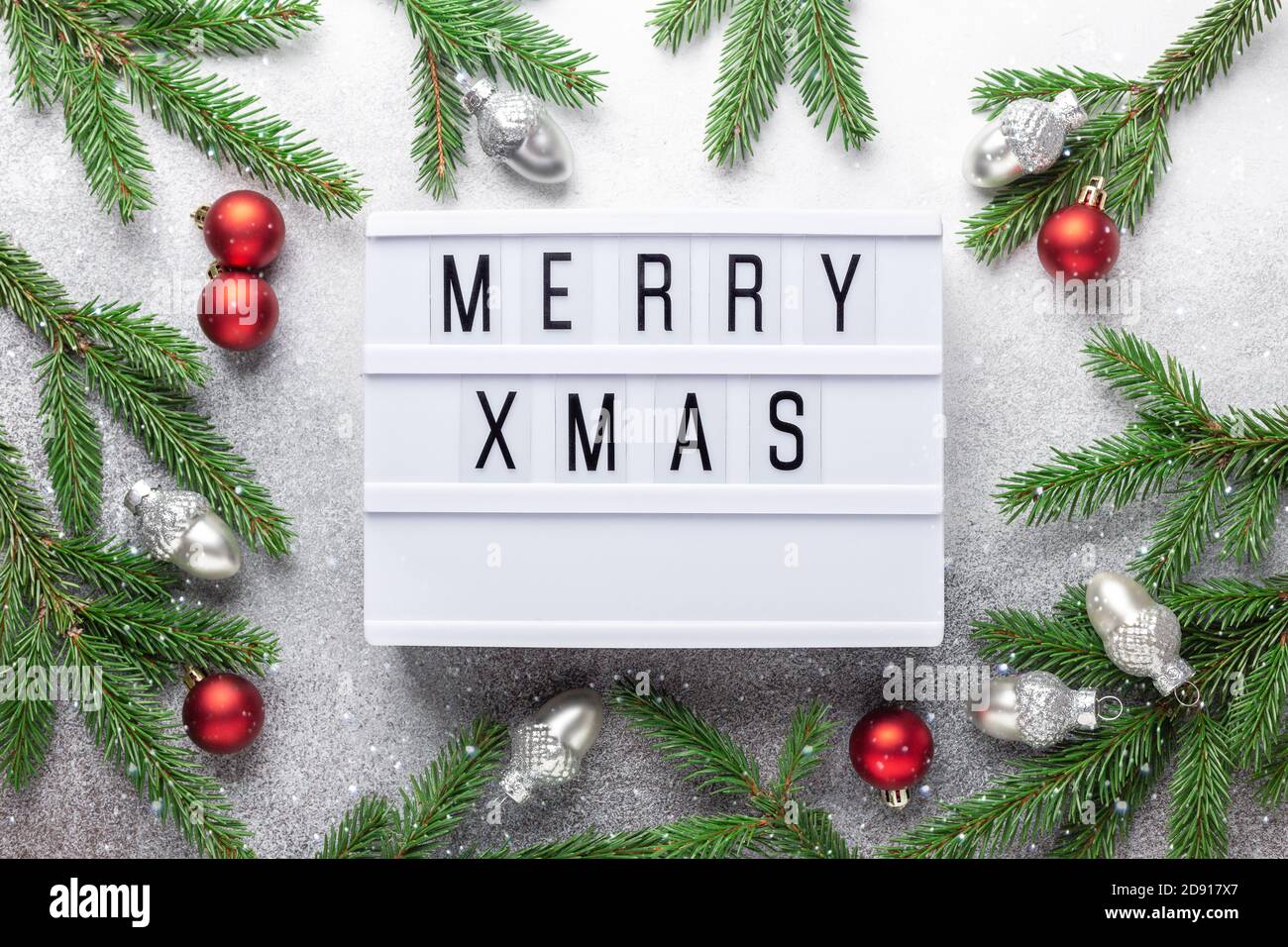 Lightbox mit Text FROHE WEIHNACHTEN, silberne und rote weihnachtskugeln und Tannenbaum Zweig auf Stein Hintergrund. Weihnachtskomposition mit Schnee-Effekt- Bild Stockfoto
