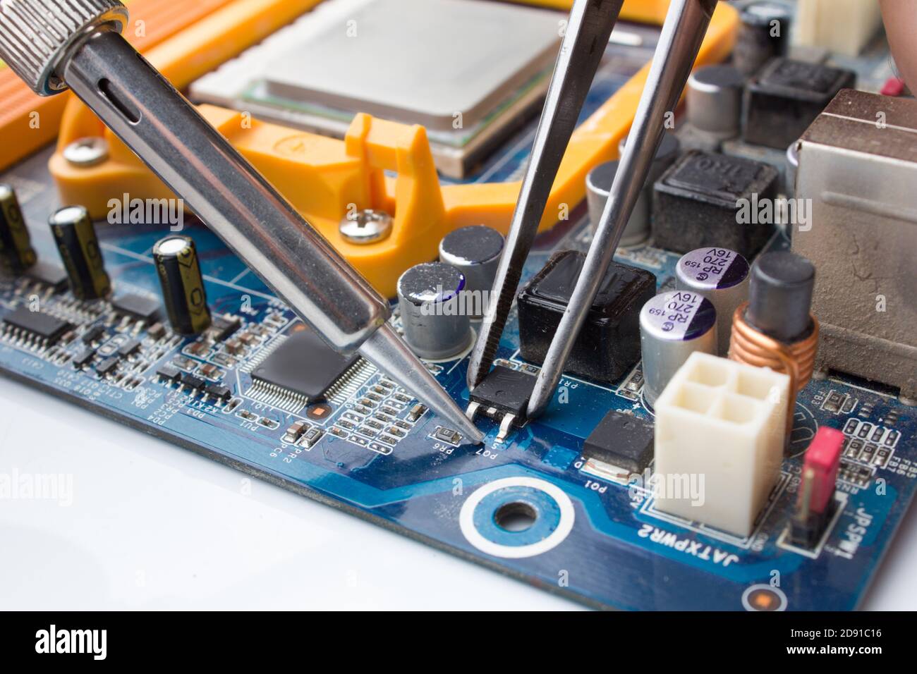 Ein MOSFET-Transistor-Schlüssel wird aus dem Computer gelötet Platine mit Lötkolben und Pinzette Stockfoto