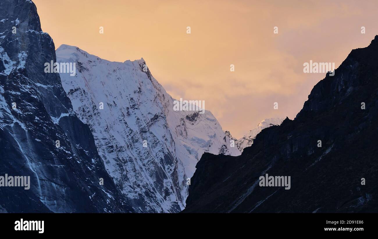 Zerklüftete Bergkette mit majestätischen eisbedeckten Bergen im Himalaya mit leicht orange gefärbten bewölkten Himmel bei Sonnenuntergang in der Nähe des Dorfes Thame, Nepal. Stockfoto