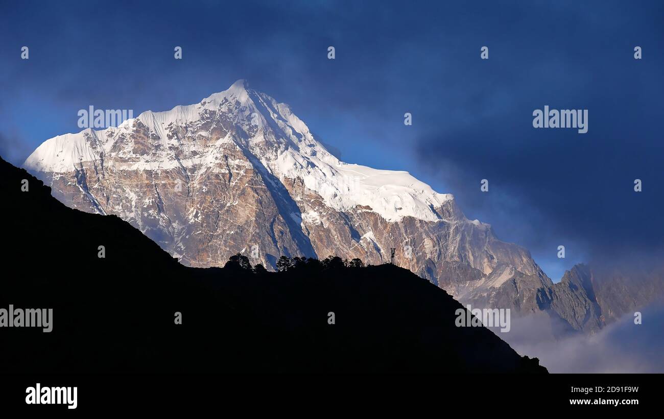 Atemberaubende Aussicht auf den majestätischen Berg Taboche (Gipfel 6,501m) Blick durch die Wolken mit Silhouette des Hügels im Vordergrund vom Mount Everest Aussichtspunkt. Stockfoto