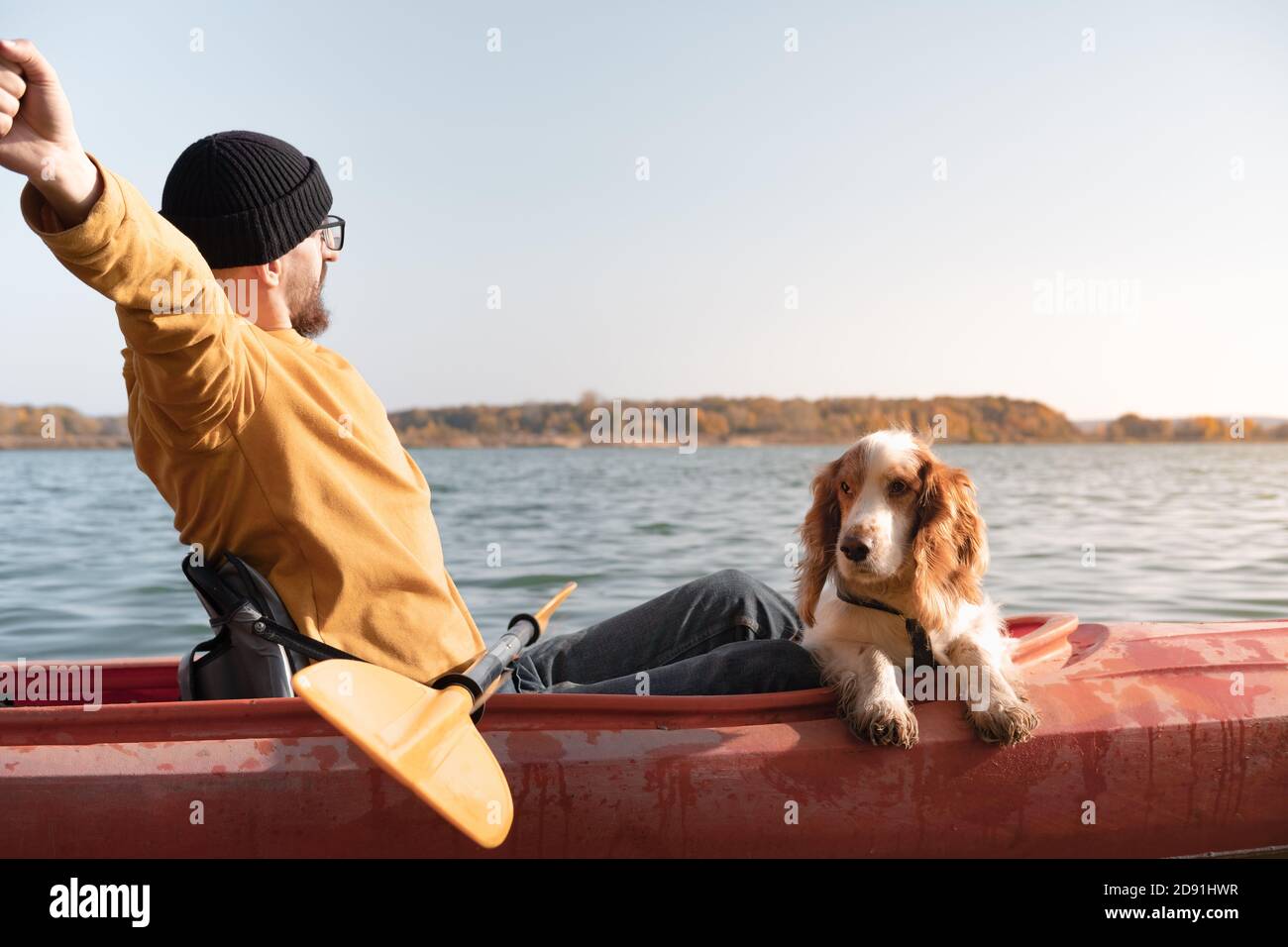 Kajakfahren mit Hunden: Der Mann streckt sich in einem Ruderboot auf dem See neben seinem Spaniel. Aktive Erholung und Abenteuer mit Haustieren, Kanu fahren mit Hund Stockfoto