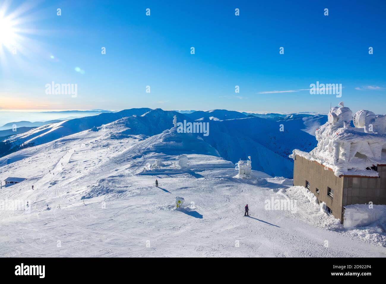 Sonne am blauen Himmel über den Wintergipfeln. Eisbedecktes Gebäude der oberen Skiliftstation Stockfoto