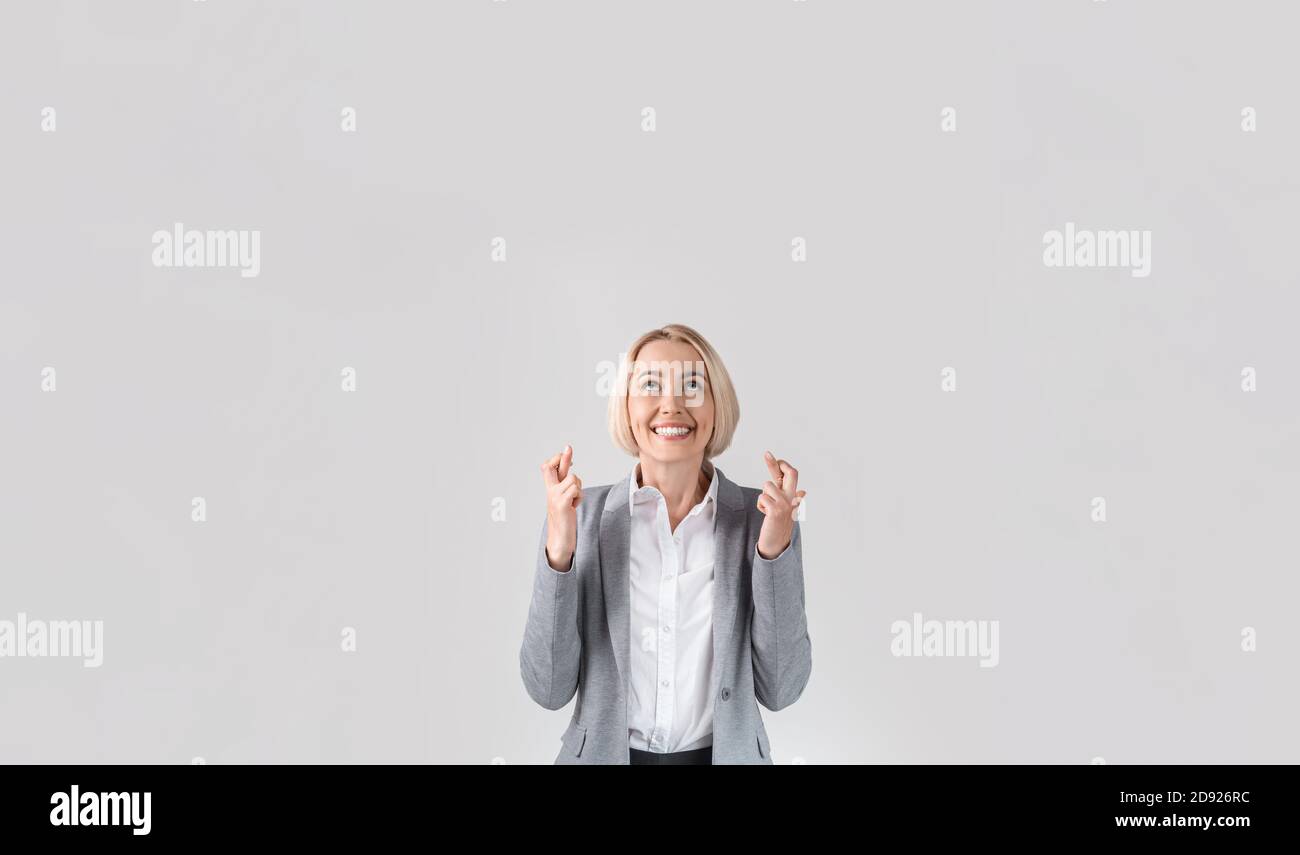 Happy blonde Geschäftsfrau in formellen Anzug Überkreuzung Finger für viel Glück auf hellgrauen Studio-Hintergrund, kopieren Raum Stockfoto