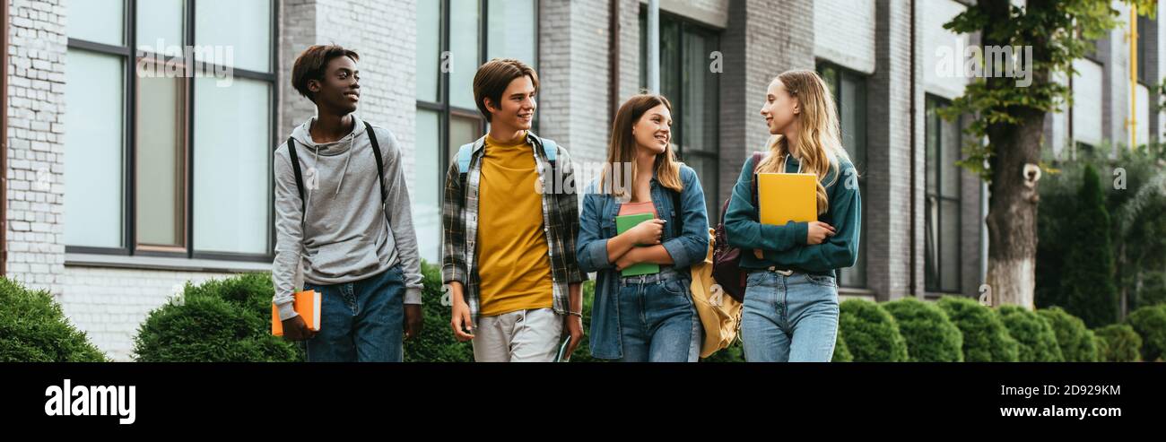Panorama-Aufnahme von lächelnden multikulturellen Teenagern mit Notebooks zu Fuß An der Stadtstraße Stockfoto