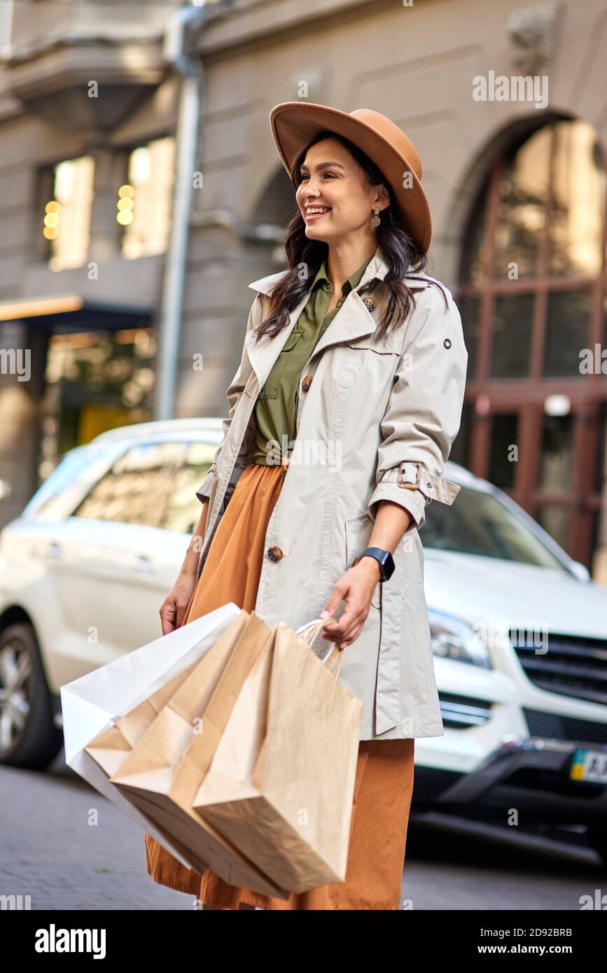 Junge glücklich schöne und stilvolle kaukasische Frau Einkaufstaschen tragen Herbst grauen Mantel und Hut Blick zur Seite und lächelnd, während auf der Straße der Stadt stehen. Shopaholism, Mode, Menschen Lebensstil Stockfoto