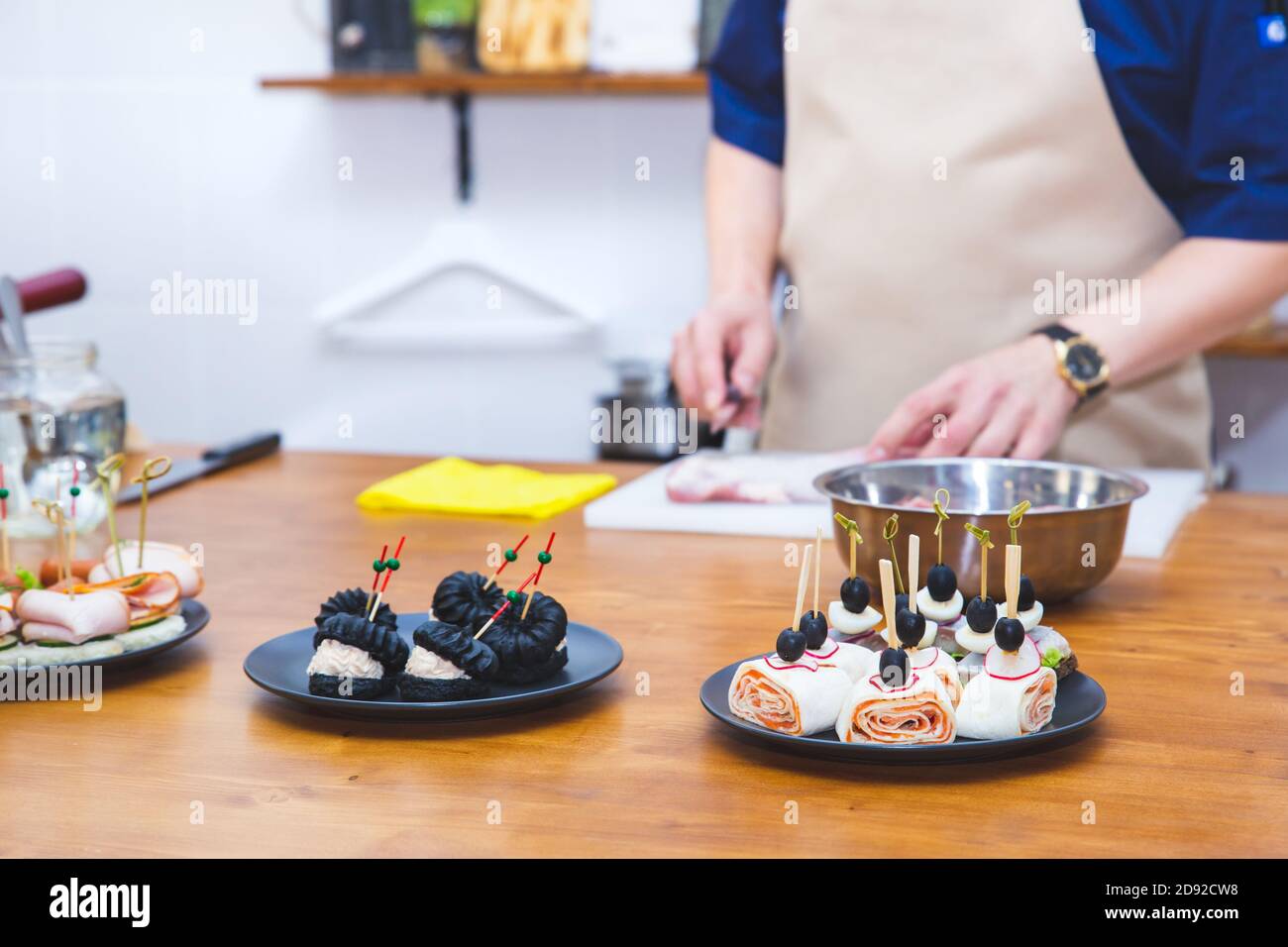 Küche, Kochen. Snacks, Profiterolen und Lavaschwalben auf Tellern auf einem Holztisch. Der Koch bereitet Essen zu, schneidet Fleisch auf einem Schneidebrett. Kochen. Stockfoto