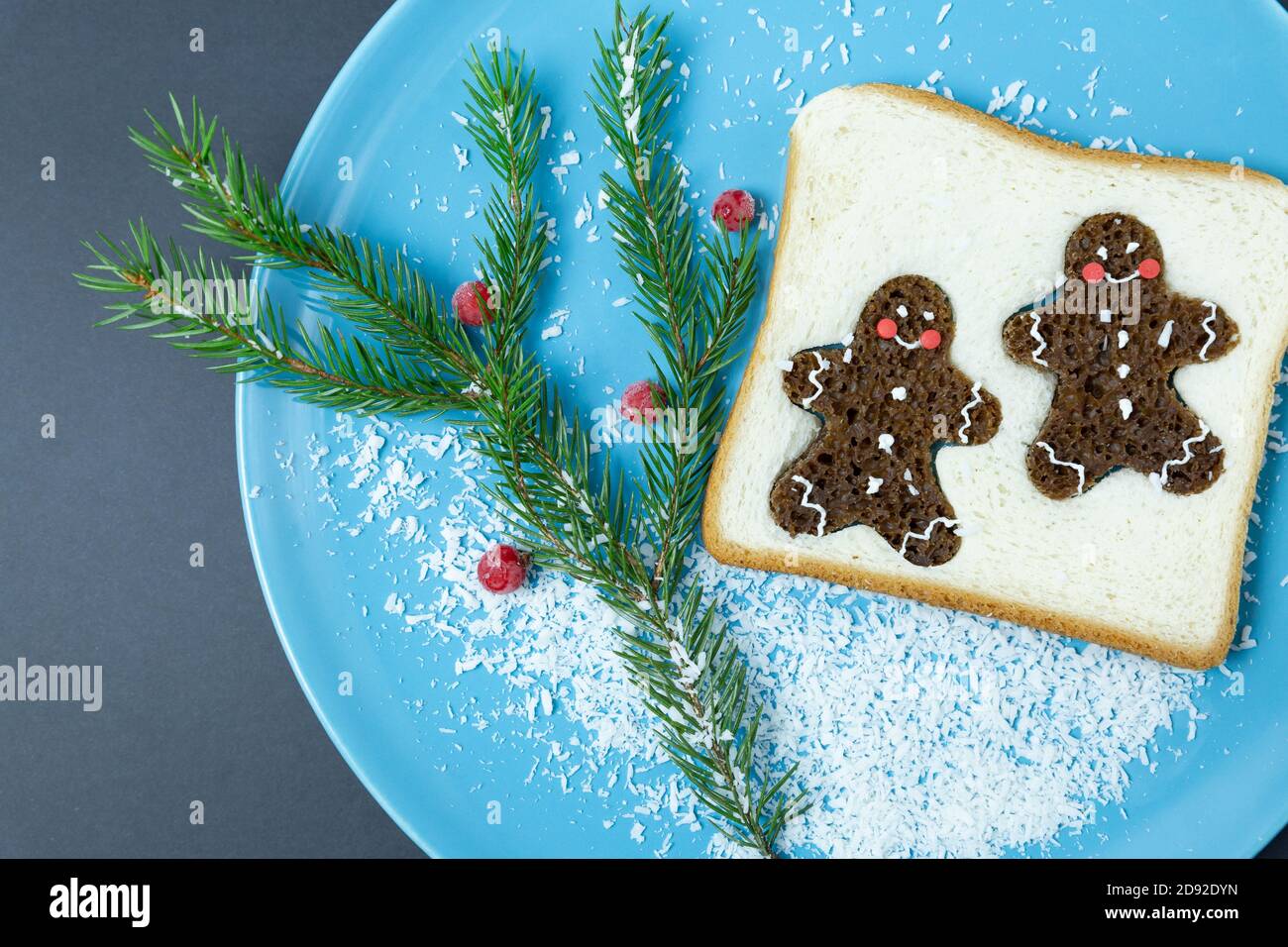 Brot Toast, verziert mit Glasur Lebkuchen Männer, gefrorene rote Johannisbeeren, Fichtenzweig auf einem blauen Teller, auf einem dunklen Hintergrund. Weihnachten, Neujahr. Fest Stockfoto