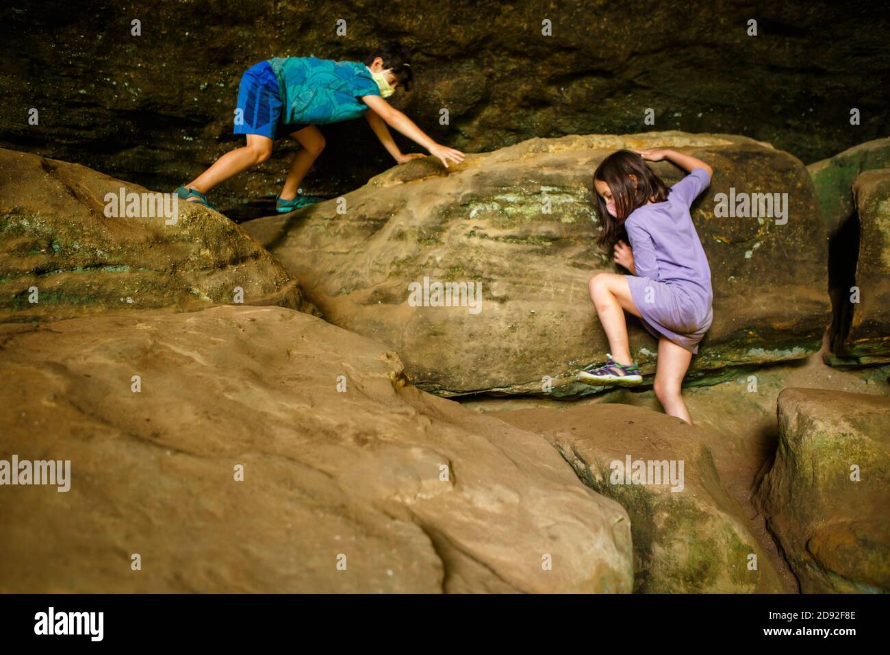 Zwei Kinder mit Gesichtsmasken klettern über große Sandsteinbrocken Stockfoto