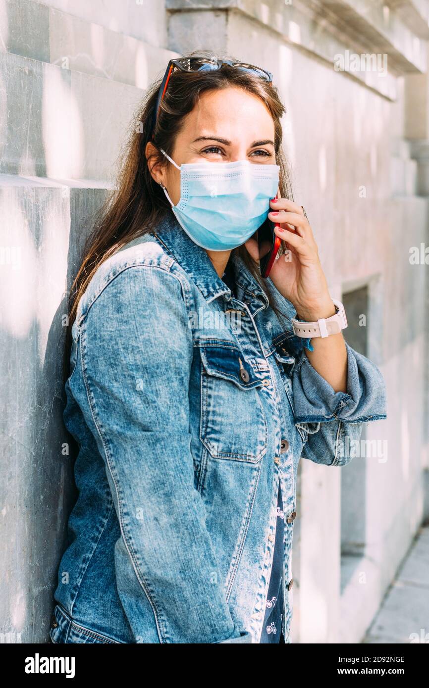 Glückliche Frau mit Gesichtsmaske spricht am Telefon Während wir die Straße hinunter gingen Stockfoto