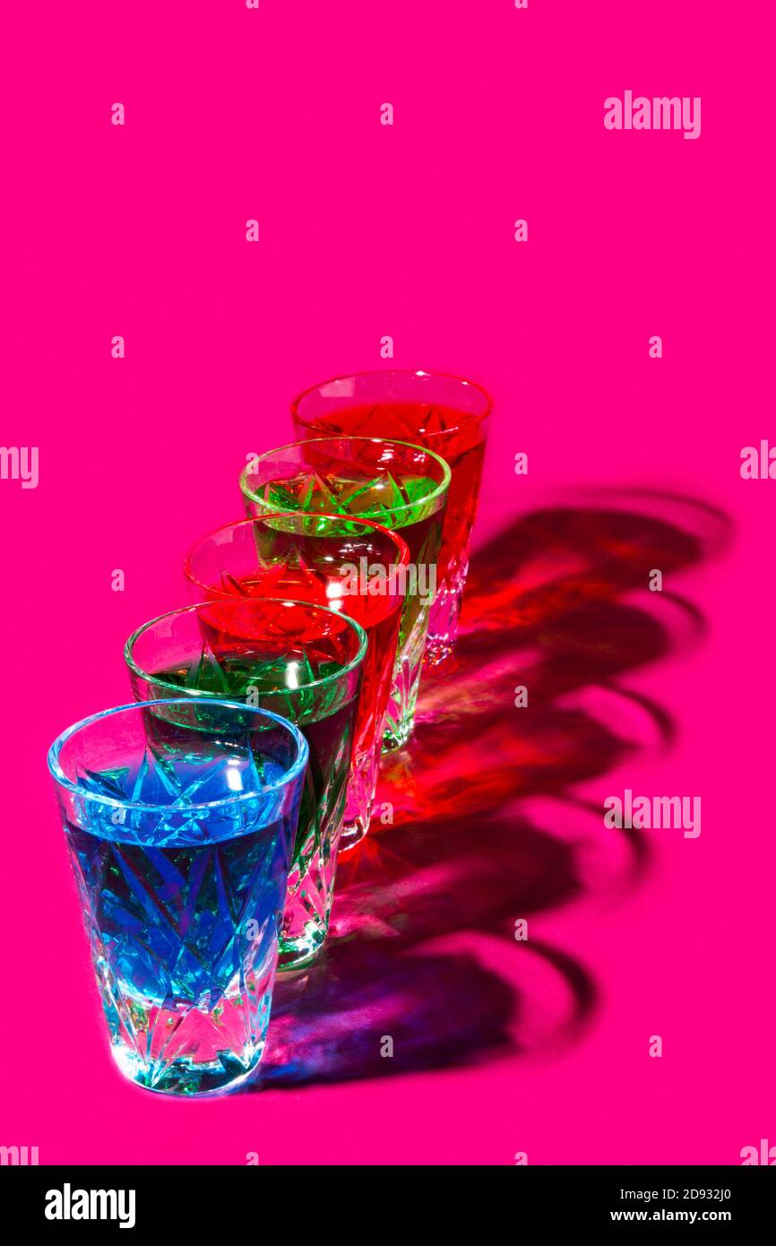 Bunte Schnapsgläser mit starkem Alkohol auf rosa Hintergrund Stockfoto