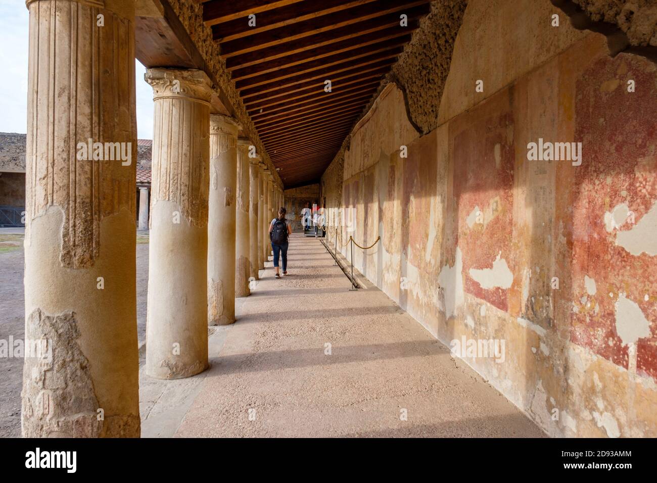 Touristen, die zwischen den Säulen vor dem Stabian Baths (Terme Stabiane) Badehaus, alten römischen Badekomplex Ruinen, Pompeji, Kampanien, Italien laufen Stockfoto