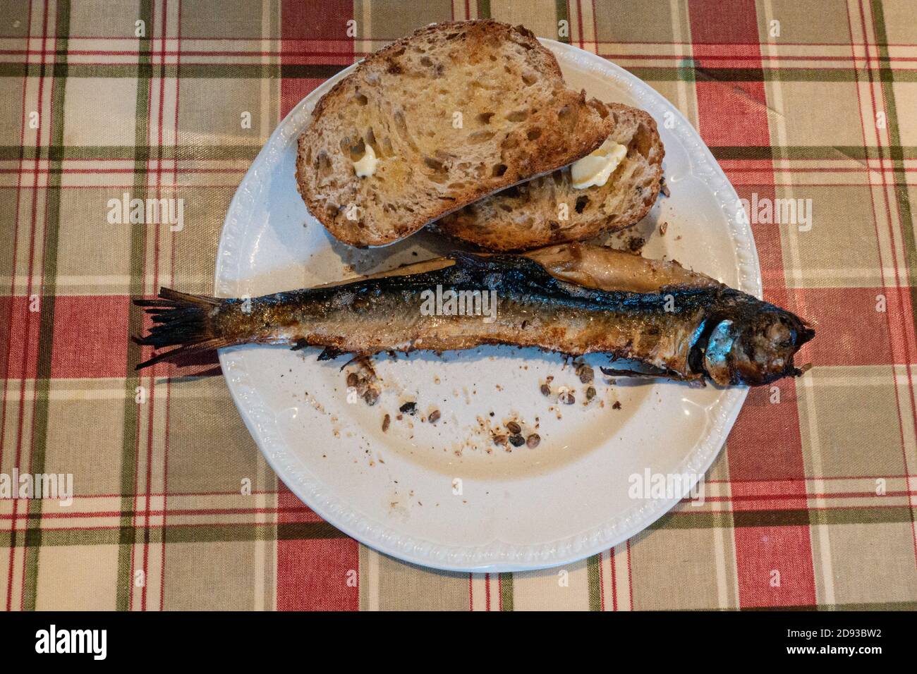 Ganzer geräucherter Fisch (Schellfisch), bekannt als Arbroath Smokies oder kipper, auf einem Teller mit gebuttertem Sauerteig-Toast auf einer Tartan-Tischdecke, Schottland, Großbritannien Stockfoto