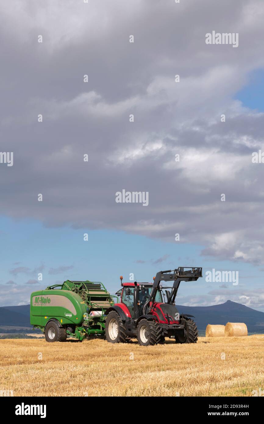 Ein Red Valtra Traktor und McHale Fusion Vario Ballenpresse in Betrieb In Aberdeenshire mit Bennachie Visible in The Distance Stockfoto