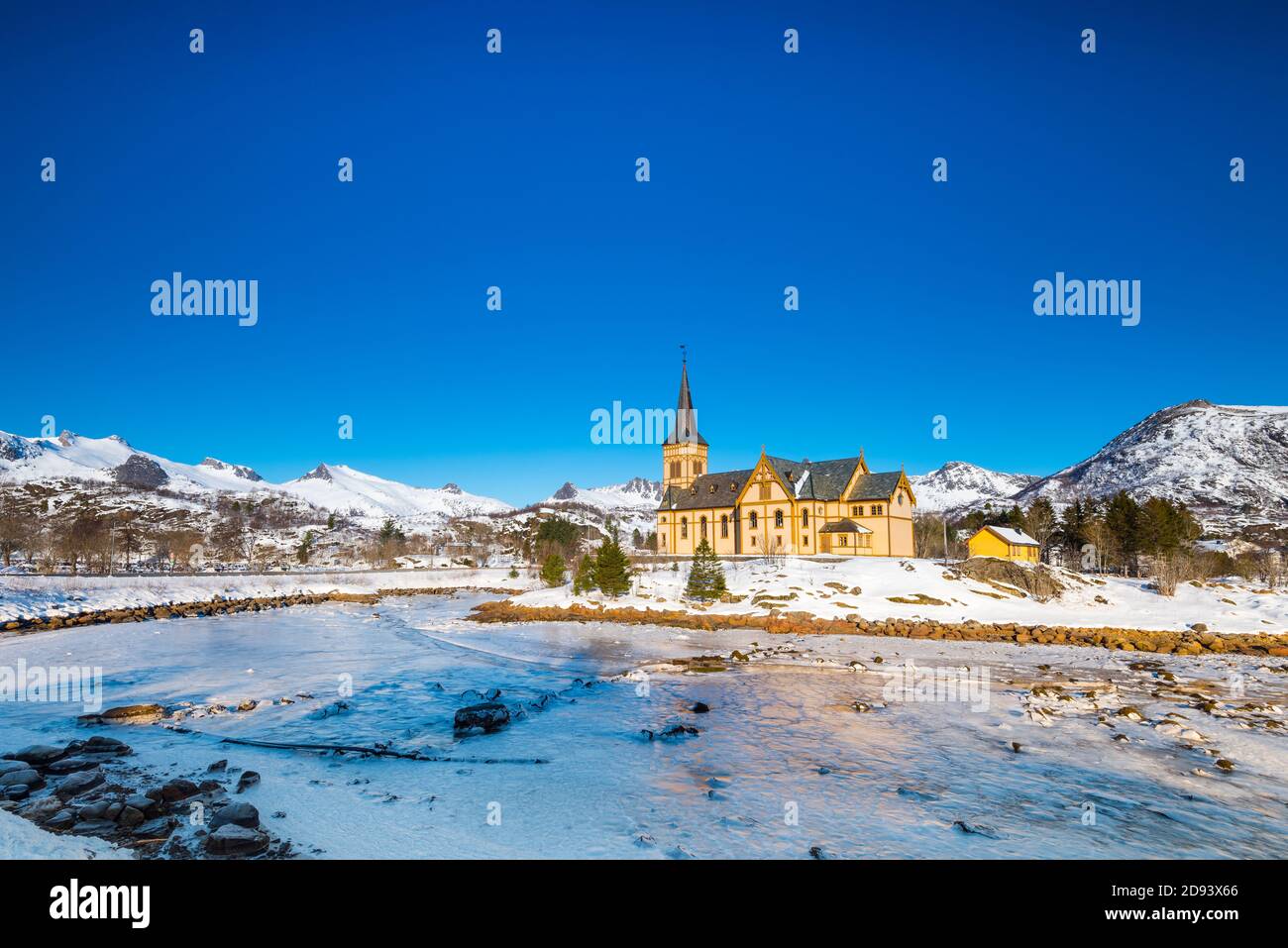 Die hölzerne gelbe Vågan Kirche am Strand auf dem Lofoten Inseln in Norwegen im Winter mit gefrorenen Fluss und Berge im Morgenlicht Stockfoto