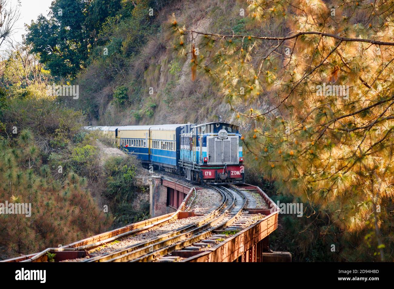 Ein sich näherender blauer indischer Dieselzug auf Eisenbahngleisen über eine Brücke durch eine Schlucht in Himachal Pradesh, Nordindien Stockfoto