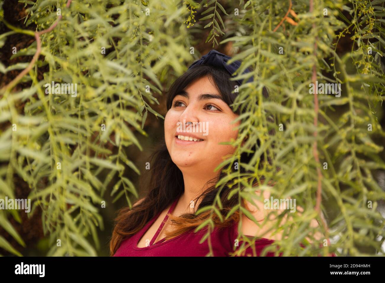 Hispanische Frau lächelt inmitten von Zweigen mit grünen Blättern Stockfoto