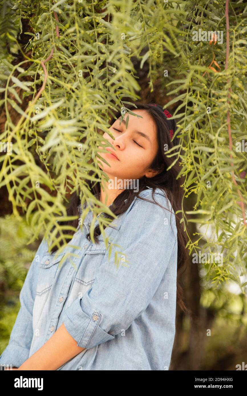 Hispanische Frau umgeben von grünen Zweigen genießen im Freien Stockfoto