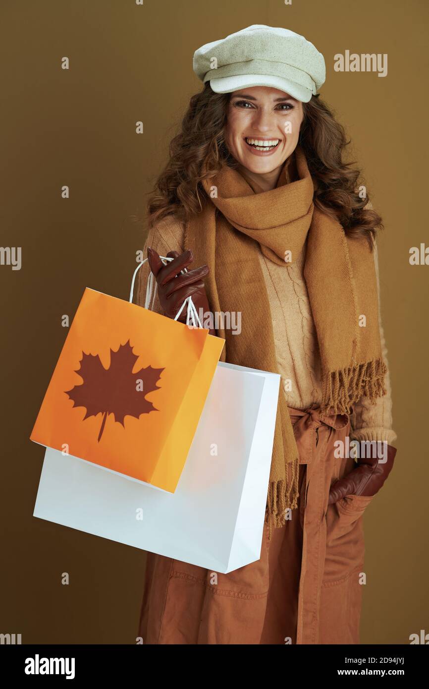 Hallo november. Glücklich stilvolle 40 Jahre alte Frau in Pullover mit Lederhandschuhen und Papier Einkaufstasche isoliert auf braunem Hintergrund. Stockfoto