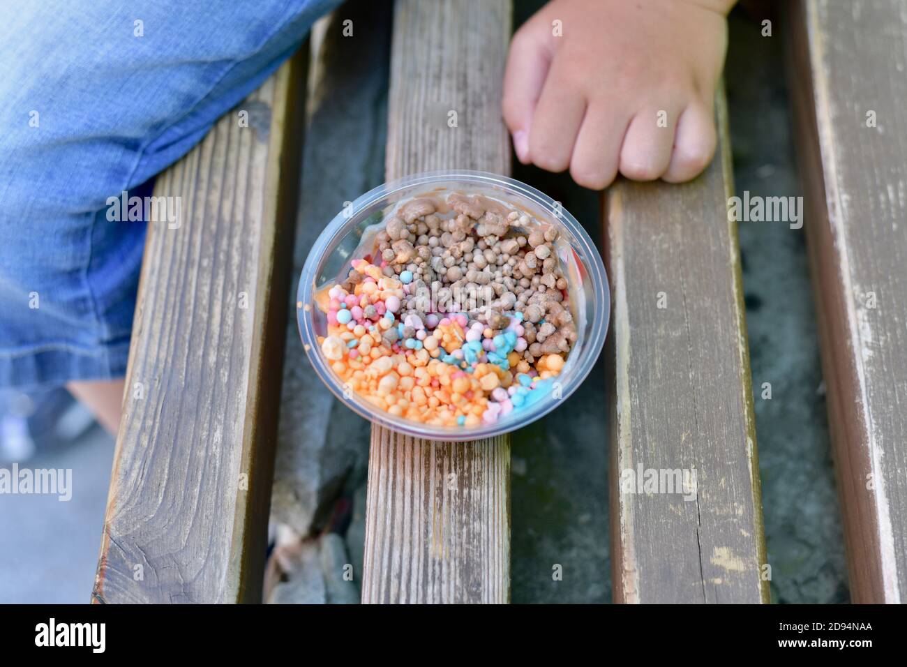 Kleine Eiscreme bunte Eiskugeln in einer Tasse auf einer Bank. Neben der Hand des Kindes. Stockfoto