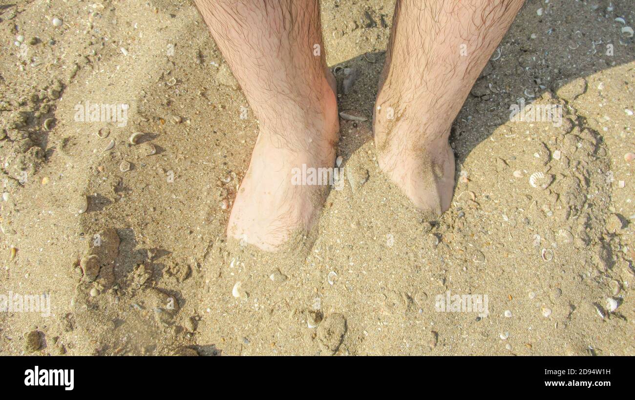 Weiße männliche Füße halb begraben unter dem Meersand Stockfoto