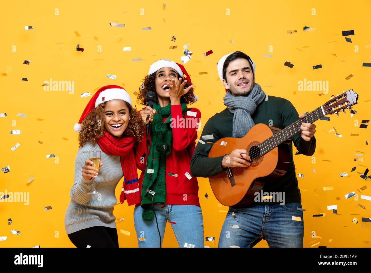 Fröhliche, vielfältige Freunde, die Party singen und Weihnachten feiern Gelber Studiohintergrund mit Konfetti Stockfoto