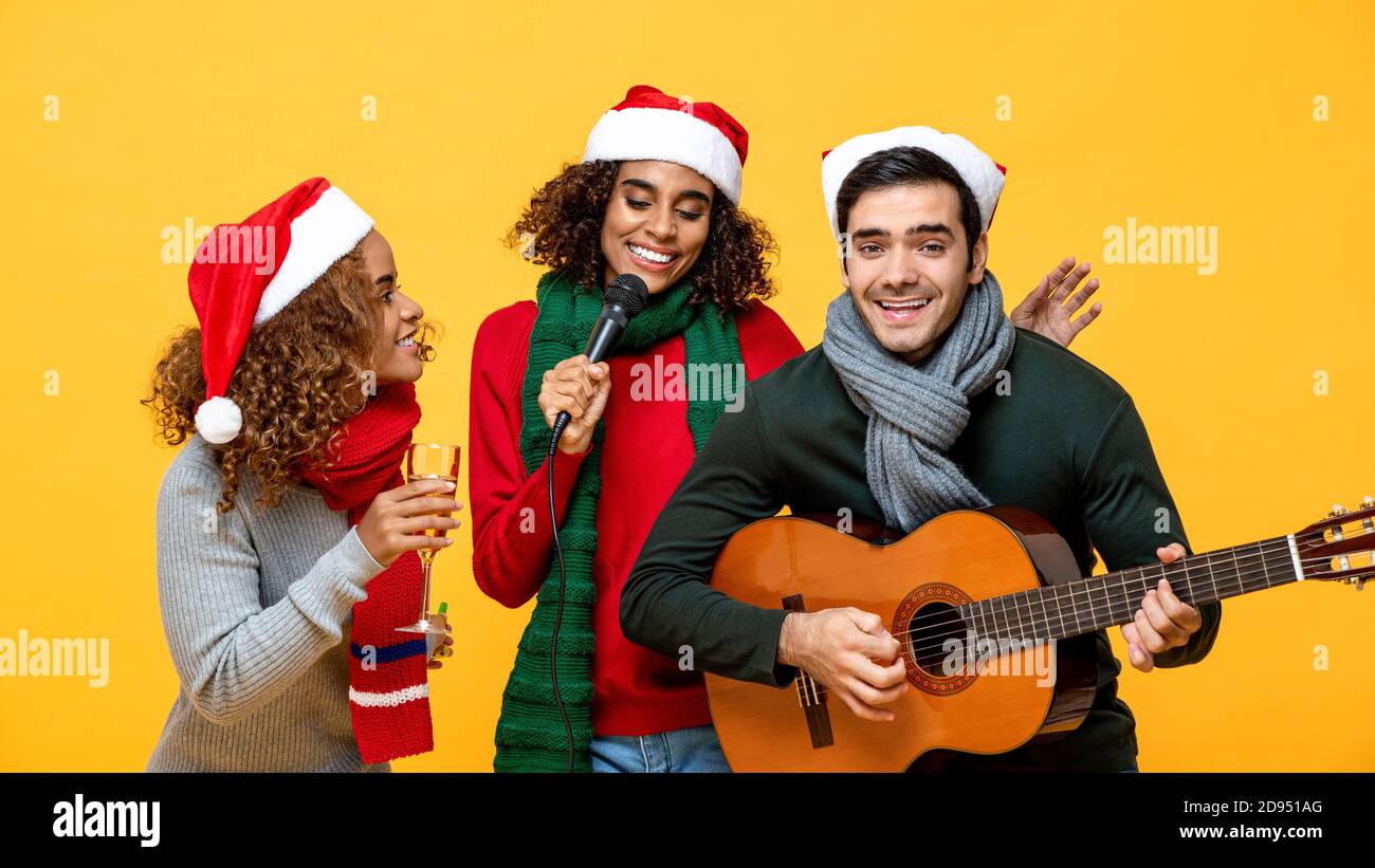 Fröhliche, vielfältige Freunde, die Party singen und Weihnachten feiern Gelber Studiohintergrund Stockfoto