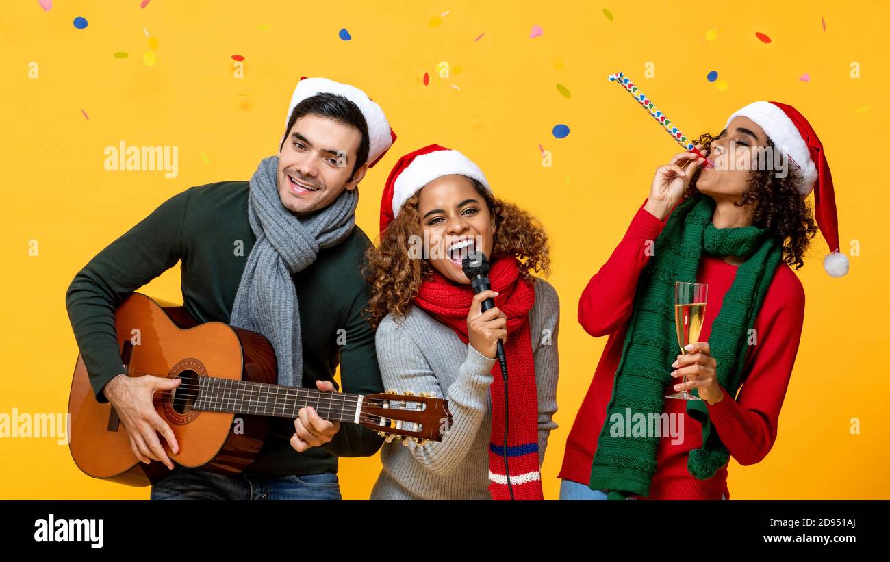 Fröhliche, vielfältige Freunde, die Party singen und Weihnachten feiern Gelber Studiohintergrund mit bunten Konfetti Stockfoto