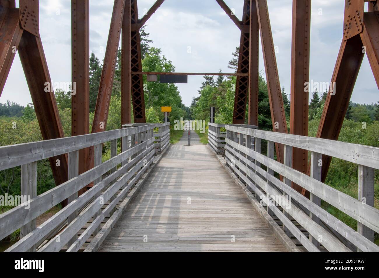 Eine Holzbrücke mit Metallstützen, die einen Fluss als Teil eines längeren geraden Weges überquert. Stockfoto