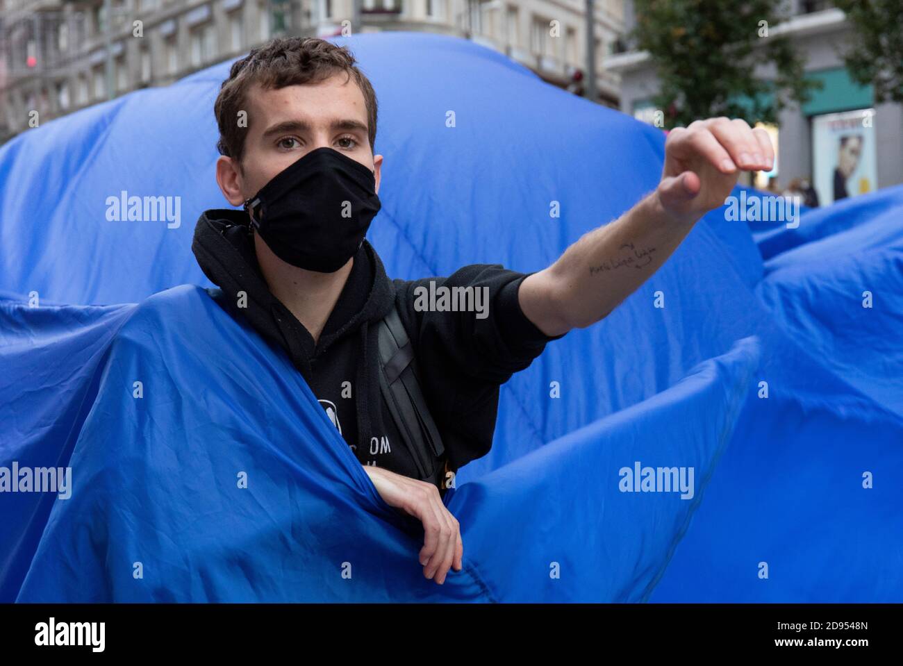 Während der Demonstration ist ein Aktivist mit Gesichtsmaske im blauen Tuch zu sehen.während der dritten internationalen Rebellion blockierte die Bewegung Extinction Rebellion die Gran Vía Straße in Madrid, um gegen die Folgen des steigenden Meeresspiegels zu protestieren. Die Bewegung, die ein 150 Quadratmeter blaues Tuch vom Callao-Platz zum spanischen Platz trägt, marschiert über die Gran Vía-Straße, um die wachsende Zahl der Menschen sichtbar zu machen, die vom Anstieg des Meeresspiegels, verursacht durch den Klimawandel, betroffen sind. Dieser Akt unter dem Namen "Wir sinken" hat die große Zahl der Todesfälle durch den Anstieg des Meeresspiegels dargestellt. Stockfoto