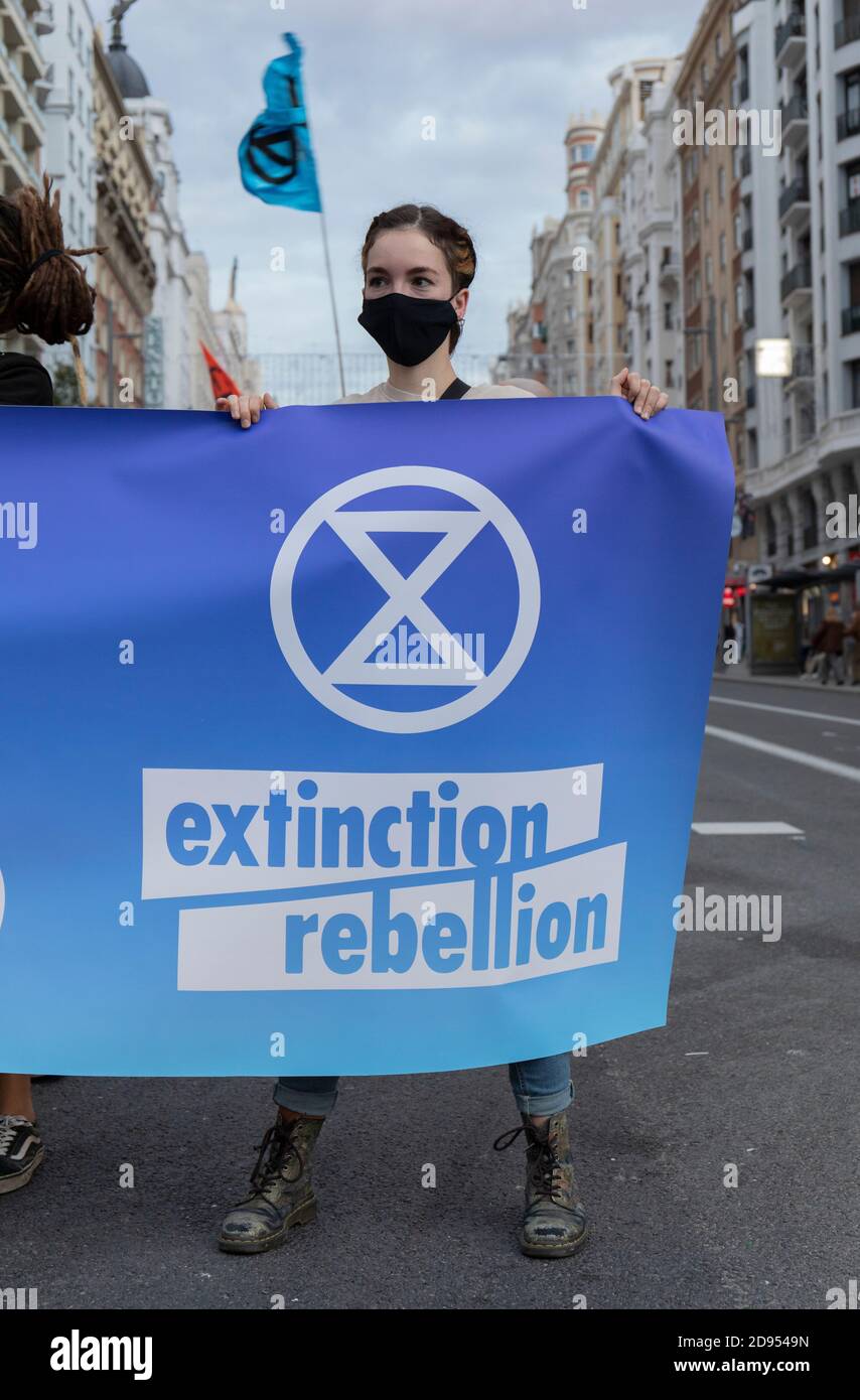 Ein Aktivist mit Gesichtsmaske hält während der Demonstration ein Banner mit dem Logo der Extinction Rebellion.während der dritten internationalen Rebellion blockierte die Extinction Rebellion Bewegung die Gran Vía Straße in Madrid, um gegen die Folgen des steigenden Meeresspiegels zu protestieren. Die Bewegung, die ein 150 Quadratmeter blaues Tuch vom Callao-Platz zum spanischen Platz trägt, marschiert über die Gran Vía-Straße, um die wachsende Zahl der Menschen sichtbar zu machen, die vom Anstieg des Meeresspiegels, verursacht durch den Klimawandel, betroffen sind. Dieser Akt unter dem Namen "Wir sinken" hat die große Zahl der Todesfälle durch den Anstieg der See dargestellt Stockfoto