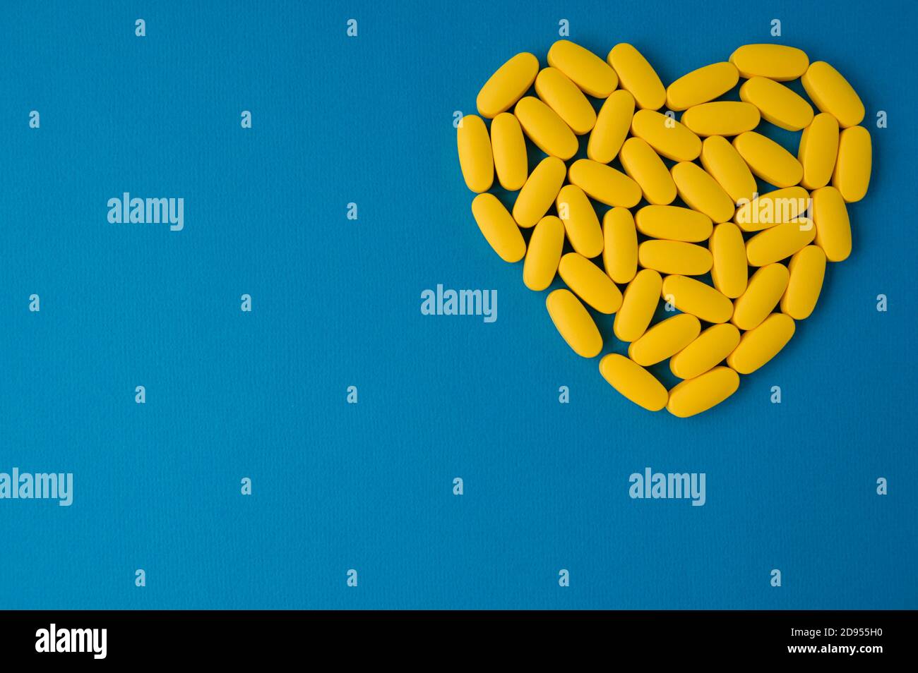 Gelbe Pillen Gesundheit Medikamente Tabletten in Herzform liegen auf Blaue, lebendige Oberfläche mit Kopierbereich Stockfoto