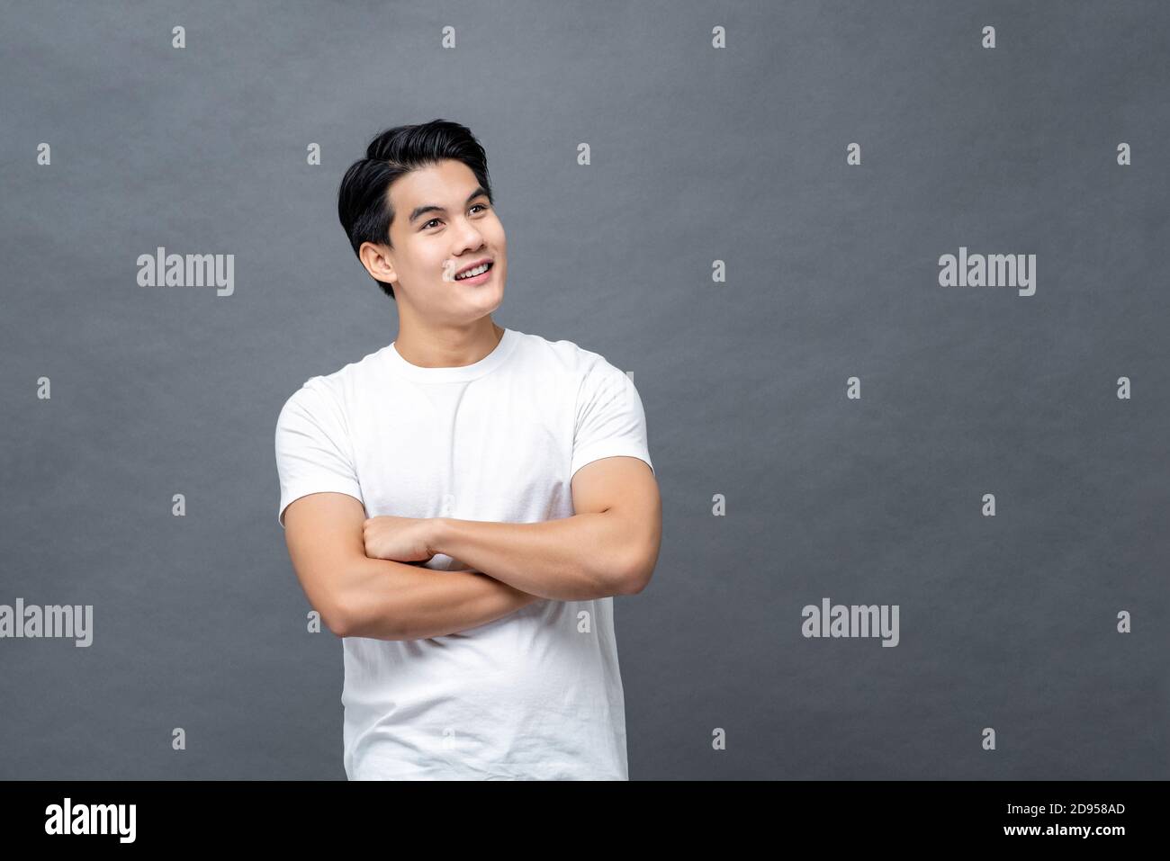 Taille bis Porträt von gut aussehend fröhlich asiatischen Mann in Armen Gekreuzte Geste Blick auf leeren Raum neben isolierten grauen Hintergrund Stockfoto