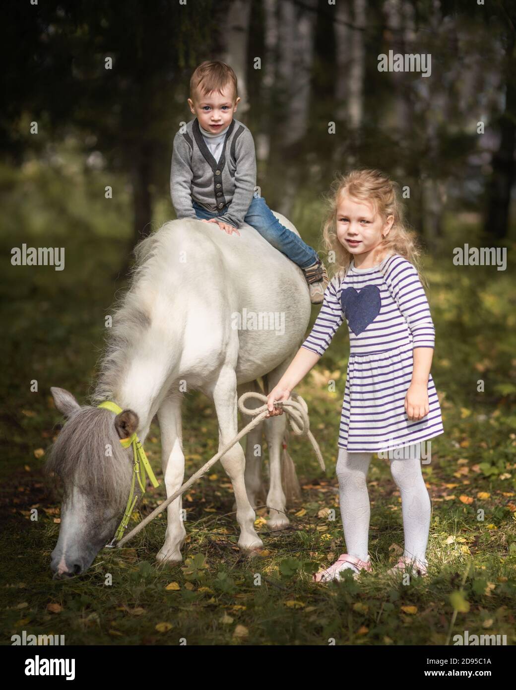Kleine blonde Mädchen führenden Pony durch Zaum mit ihrer jüngeren Bruder Stockfoto