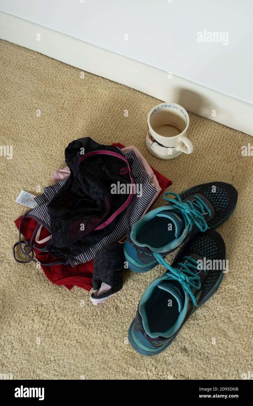 Leere Tasse und Frauenkleidung auf dem Schlafzimmerboden. Stockfoto